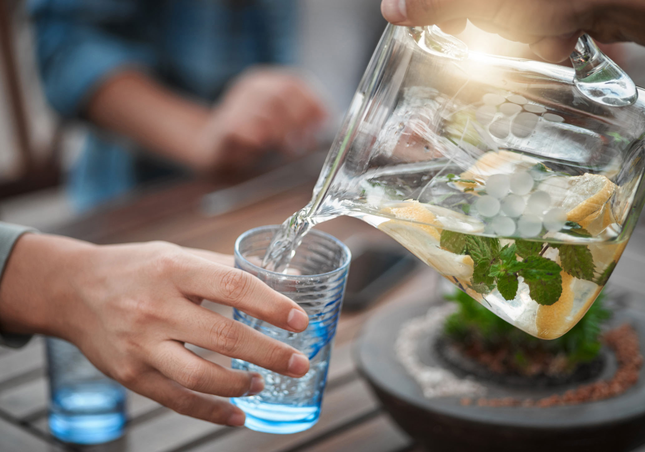 person som häller vatten ur en kanna i ett glas